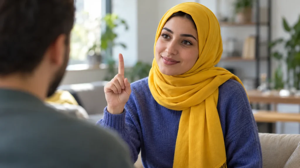 Frau mit gelbem Kopftuch sitzt einer Person gegenüber und hebt beim Gebärden den Zeigefinger.